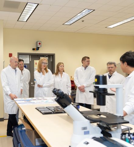 Des gens en blouse blanche debout près de microscopes dans un laboratoire.