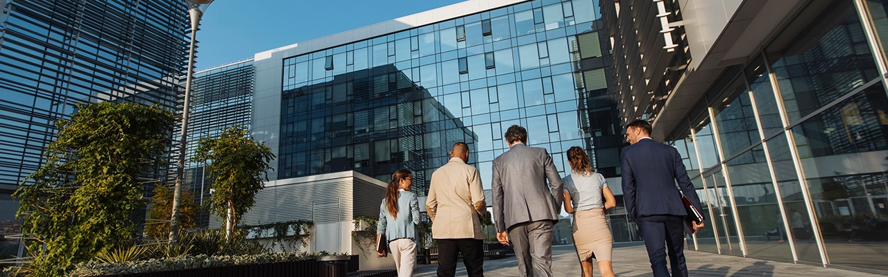 Plan arrière de cinq hommes d’affaires marchant à côté d’un immeuble de bureaux